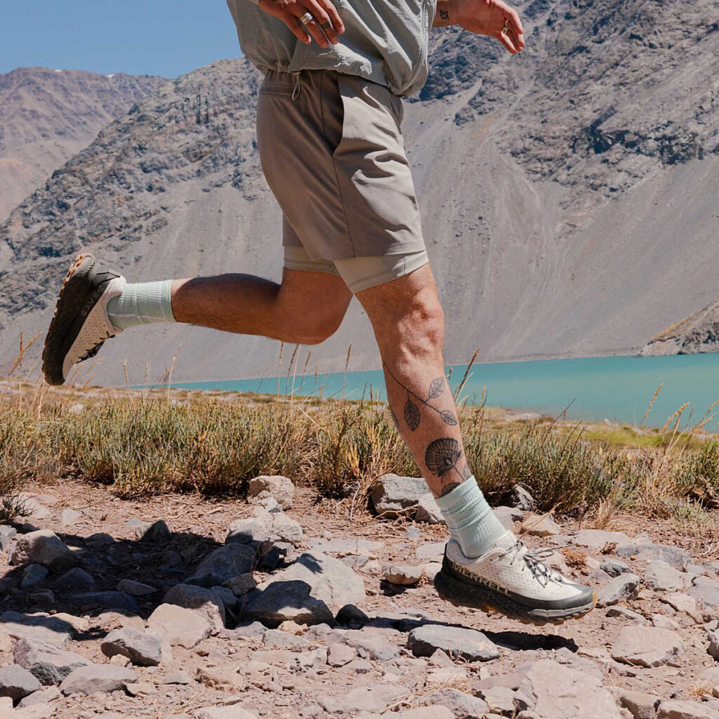 Coureur en pleine action sur un sentier rocailleux de montagne, portant la Merrell Agility Peak 5, une chaussure trail Gore tex réputée pour sa robustesse et son accroche