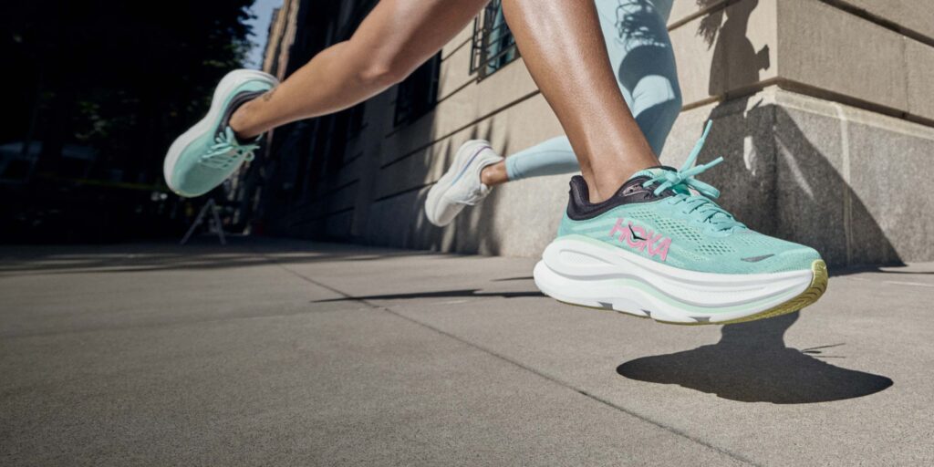 Femme courant avec des chaussures de running Hoka Bondi 9 turquoise sur route, montrant l'amorti de la semelle