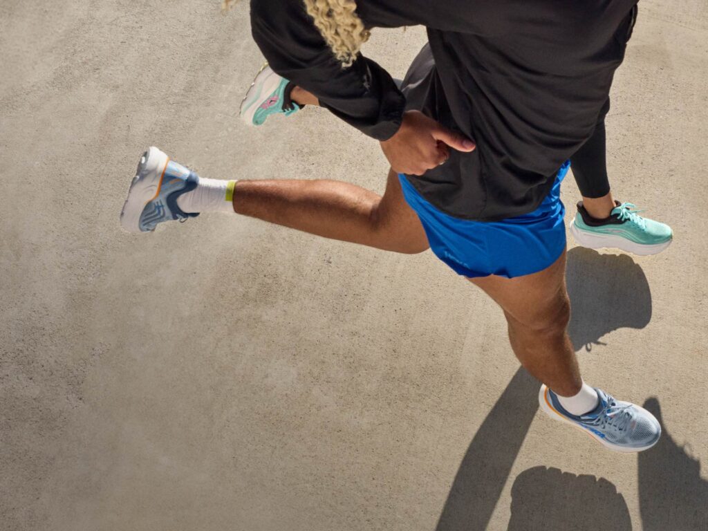 Vue de dessus de deux coureurs en pleine foulée sur le bitume, portant des chaussures de running Hoka (modèles Bondi et Clifton) et une tenue de sport